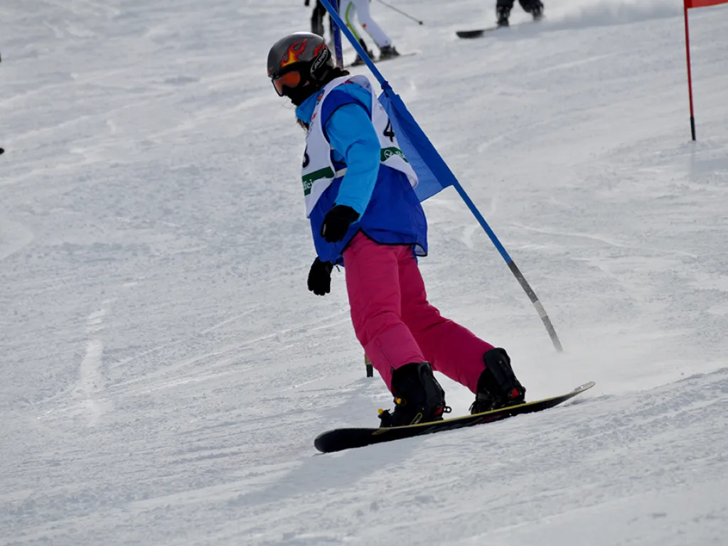 Snowboarderin in blau-pinker Kleidung umfährt ein blaues Tor.